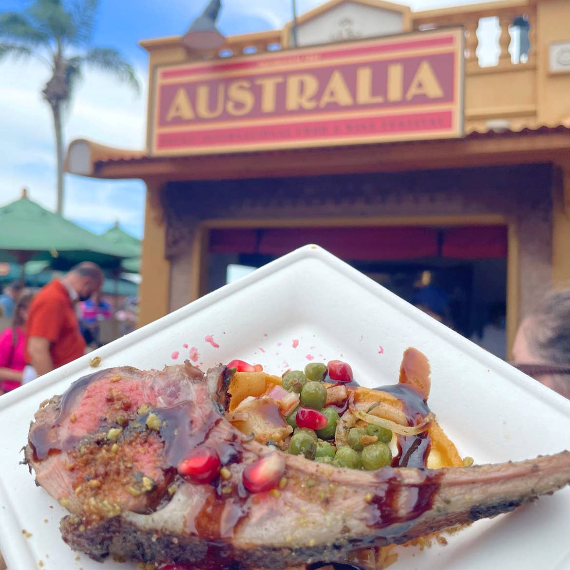 A roasted Lamb Chop with Sweet Potato Purée, Bush Berry Pea Salad, and Pistachio-Pomegranate Gremolata sits on a white, square plate near the Australia Kiosk at Epcot.