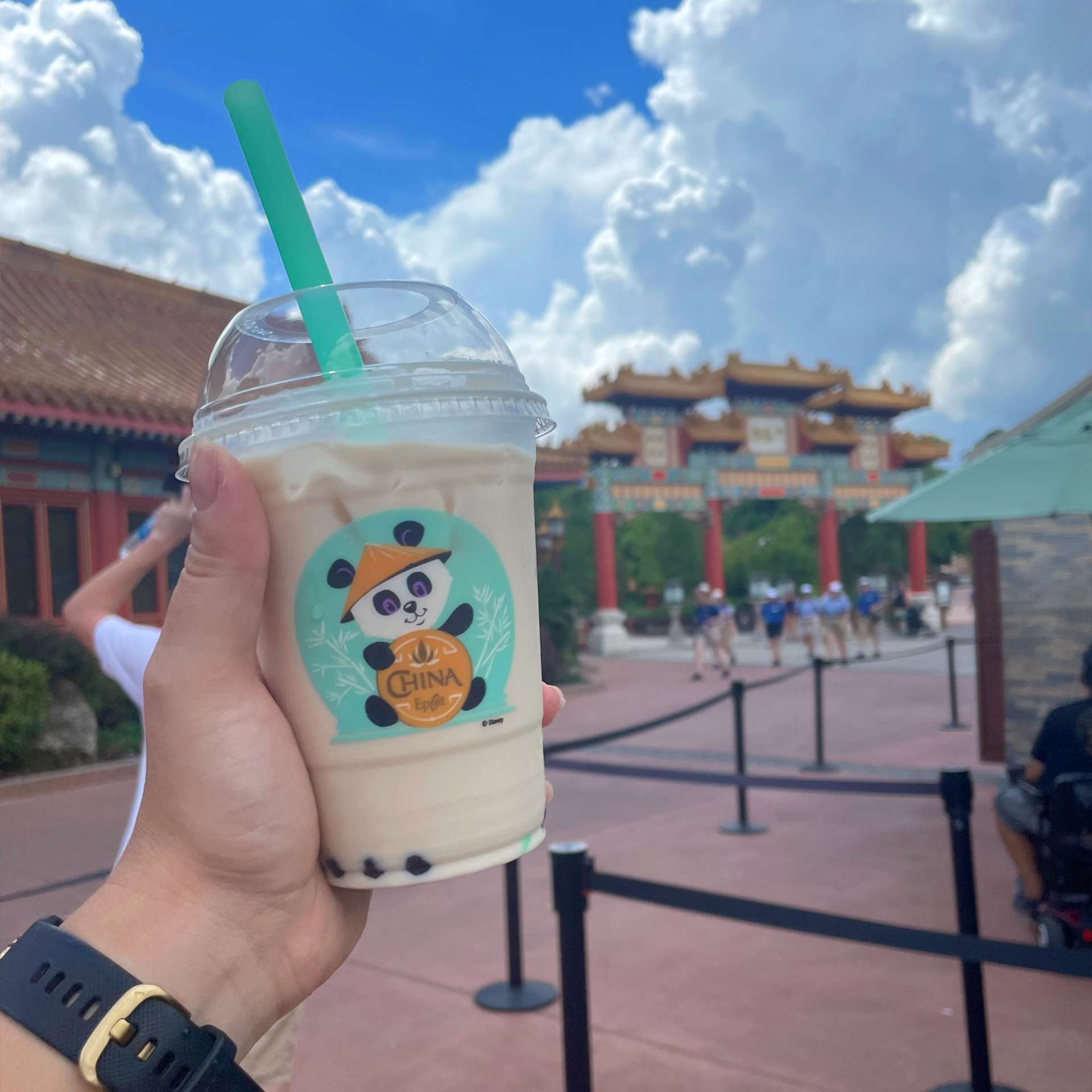 A hand holds a plastic cup of bubble tea with a panda graphic near the China Pavilion at Epcot.