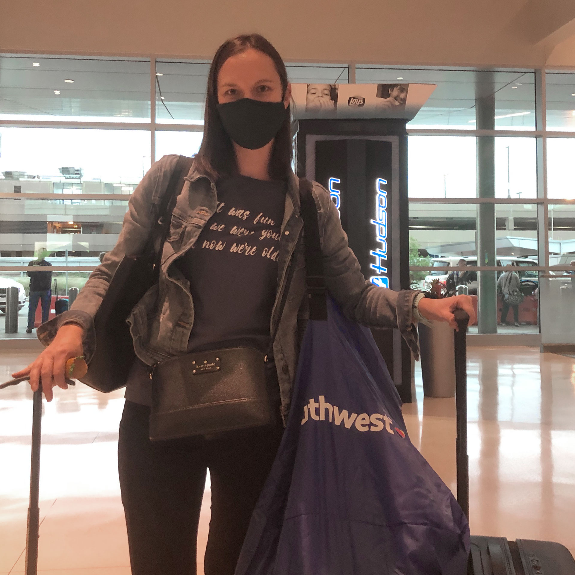 Author, Sarah, stands wearing a mask and holding several bags and suitcases containing the necessities for a safe flight.