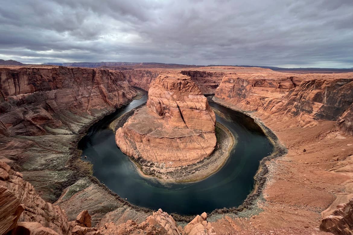 The Horseshoe Bend, where the Colorado river formed red rocks into a horseshoe formation, has dark clouds above it.
