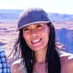 An Asian woman wearing a grey baseball cap stands in front of mountains.