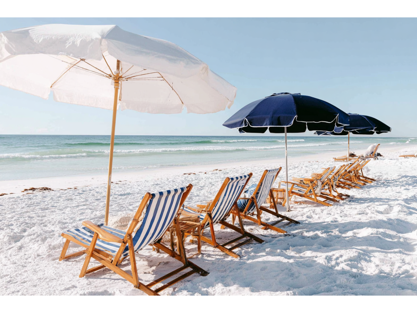 Striped beach chairs under white and navy umbrellas facing the ocean.