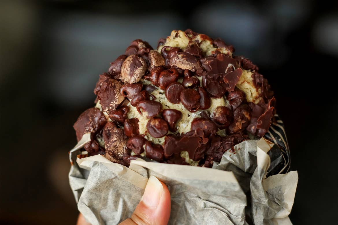 A handmade cookie coated with chocolate chips is held by a female with a napkin.