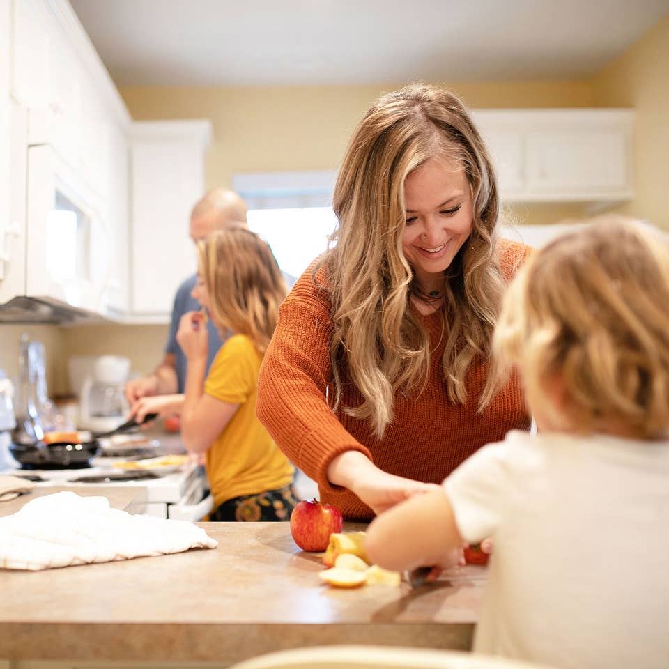 A woman in an orange sweater (front-right) helps serve a meal her husband and daughter (back-left) prepared in their Villa kitchen.