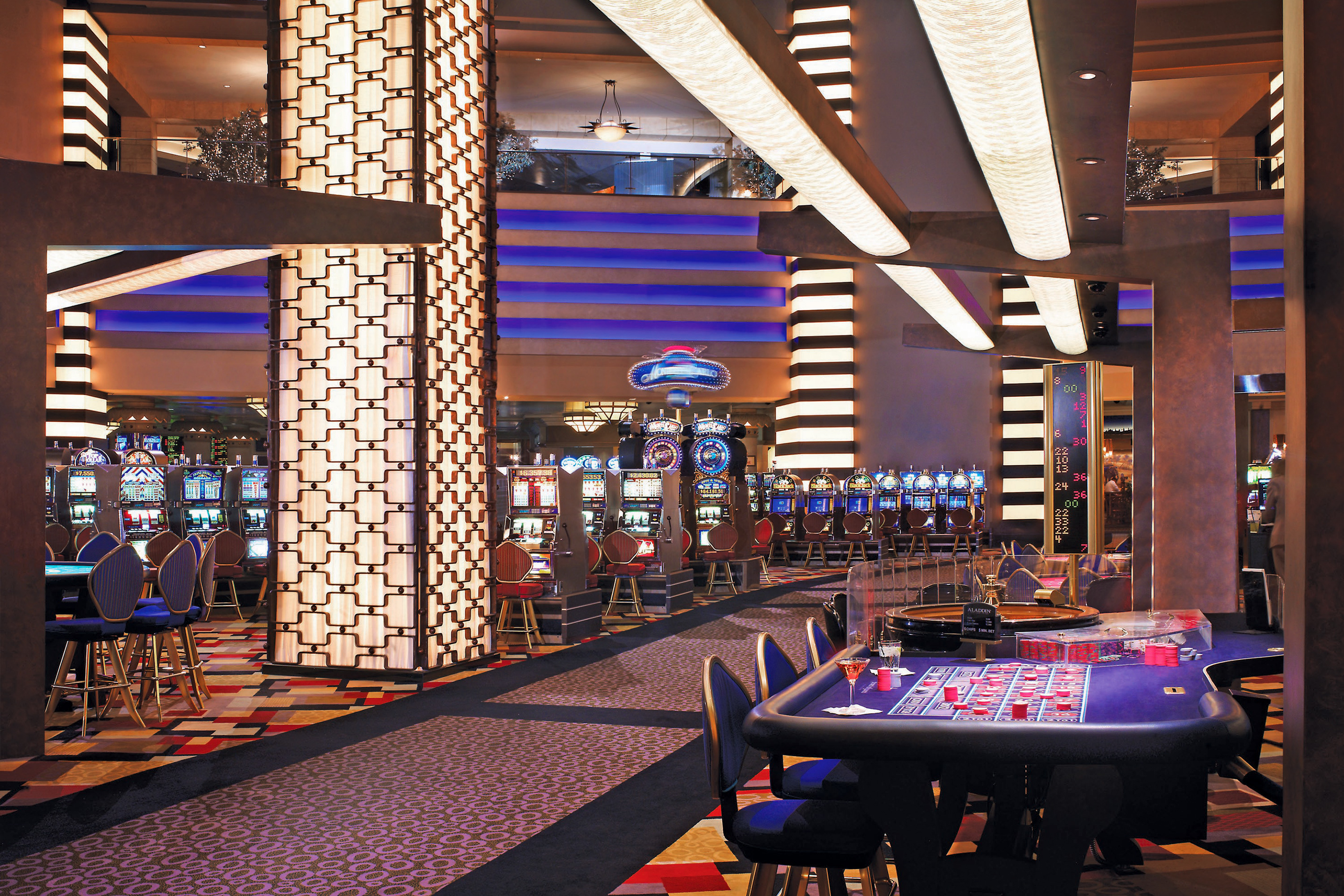 The interior of the Planet Hollywood casino floor with various lighting, digital slot machines and playing tables.