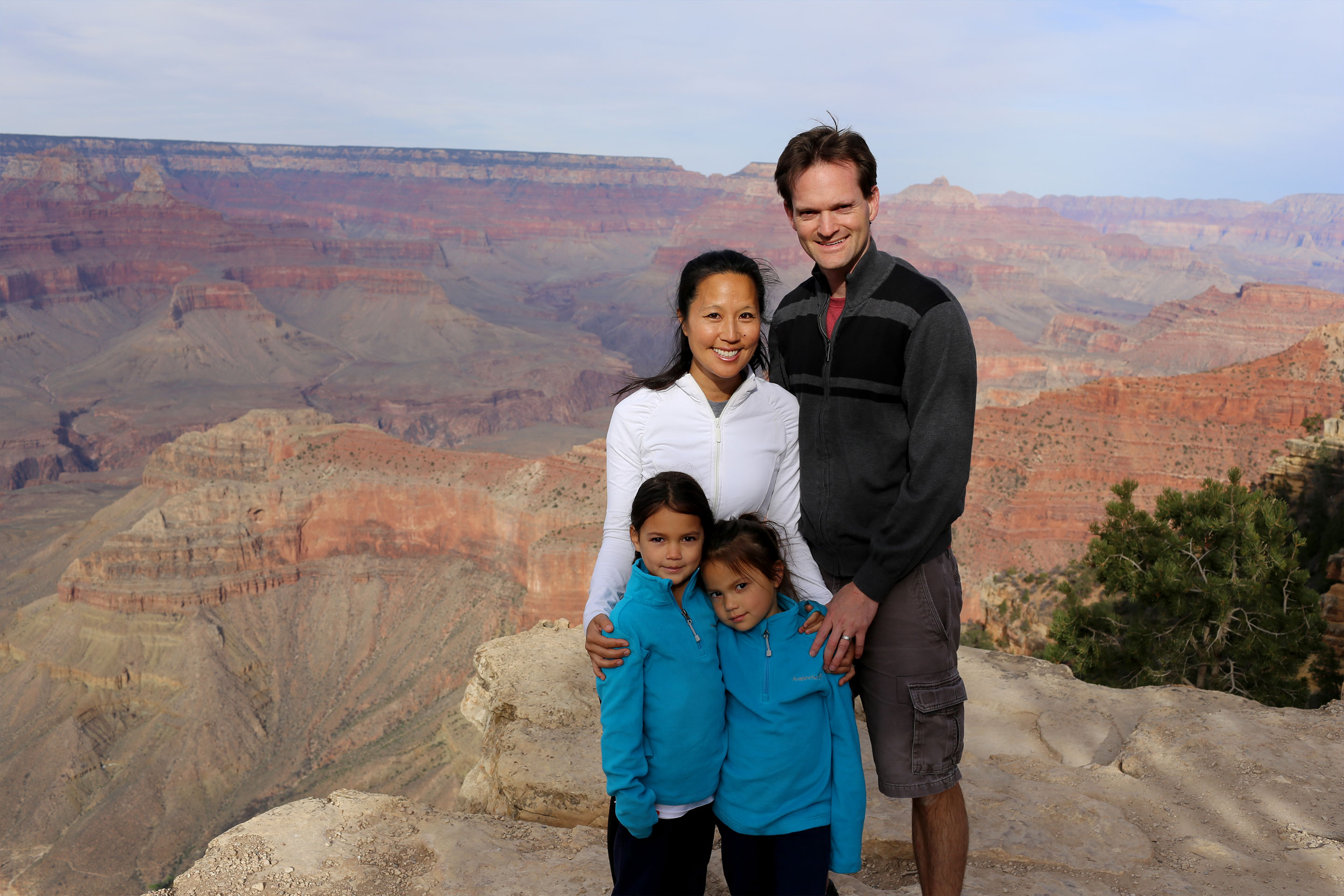 A woman, man and two young girls pose in front of the Grand Canyon wearing light jackets.