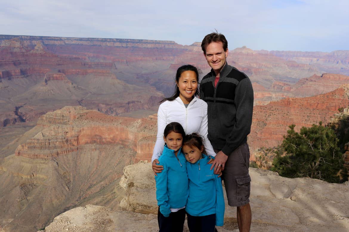 A woman, man and two young girls pose in front of the Grand Canyon wearing light jackets.