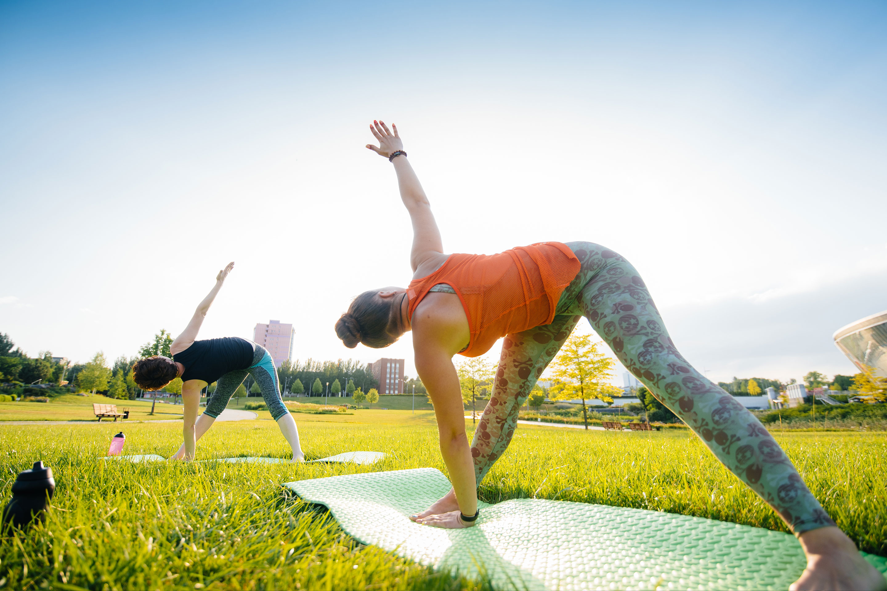 Two women doing Yoga poses on a green lawn outdoors.