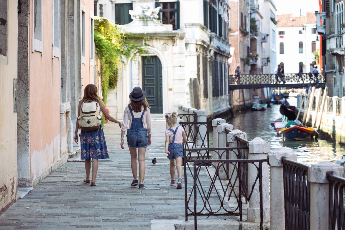A woman (left) and her two daughters (middle and far-right) walk along the riverwalk of Venice, Italy.