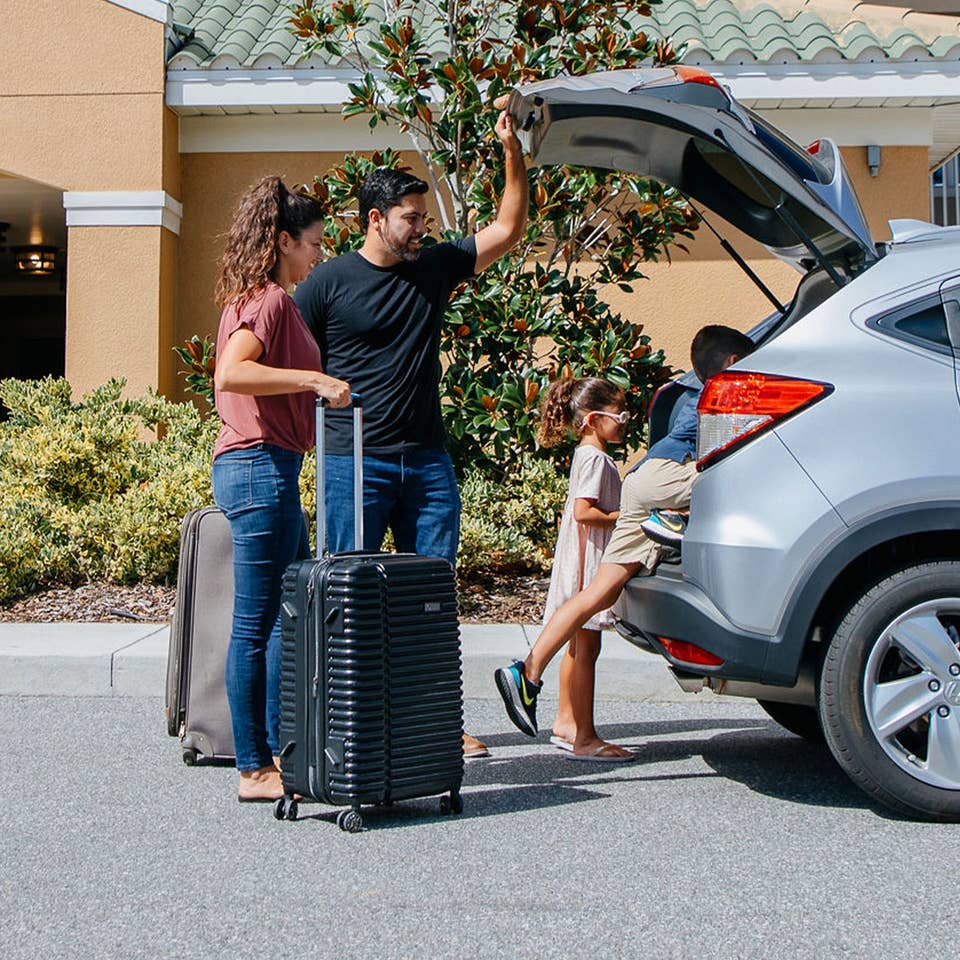 A woman, man and young boy and girl unpack a silver vehicle outside of a resort.