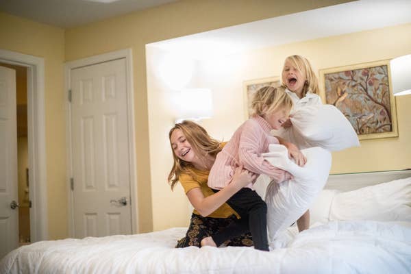 Three children laughing and having a pillow fight on a bed.