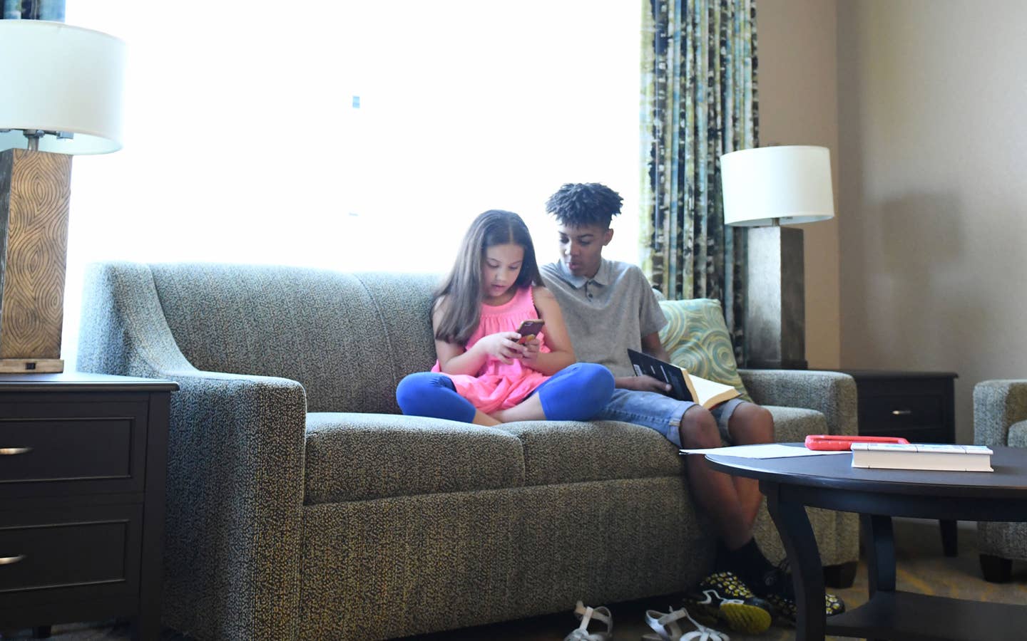 Two children sitting in a living room in a villa looking at smartphone together
