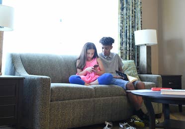 Two children sitting in a living room in a villa looking at smartphone together