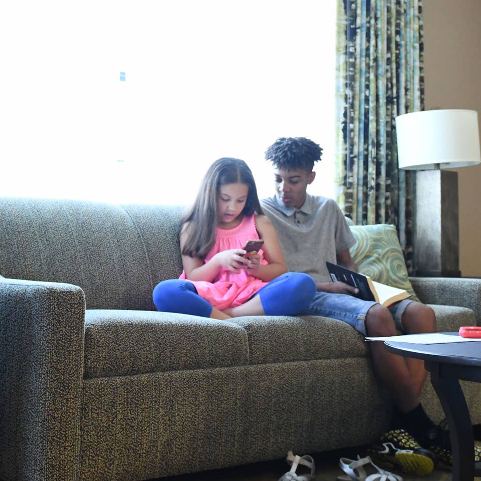 Two children sitting in a living room in a villa looking at smartphone together