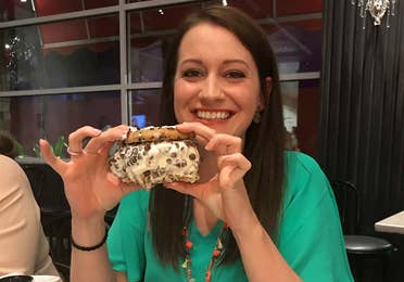A woman in a green shirt holds a large ice cream cookie sandwich in a restaurant.