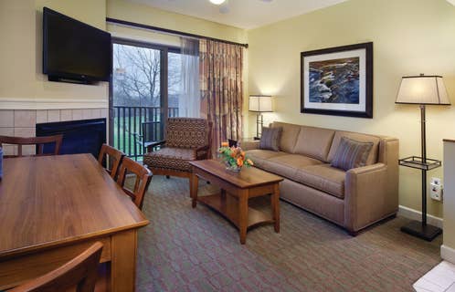Living room with couch, accent chair, fireplace and flat screen TV in a one-bedroom villa at Lake Geneva Resort