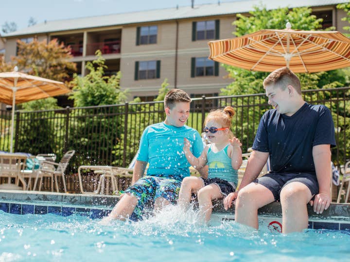 Three children sitting on edge of outdoor pool at Oak n' Spruce Resort in South Lee, Massachusetts.