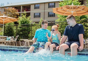 Three children sitting on edge of outdoor pool at Oak n' Spruce Resort in South Lee, Massachusetts.