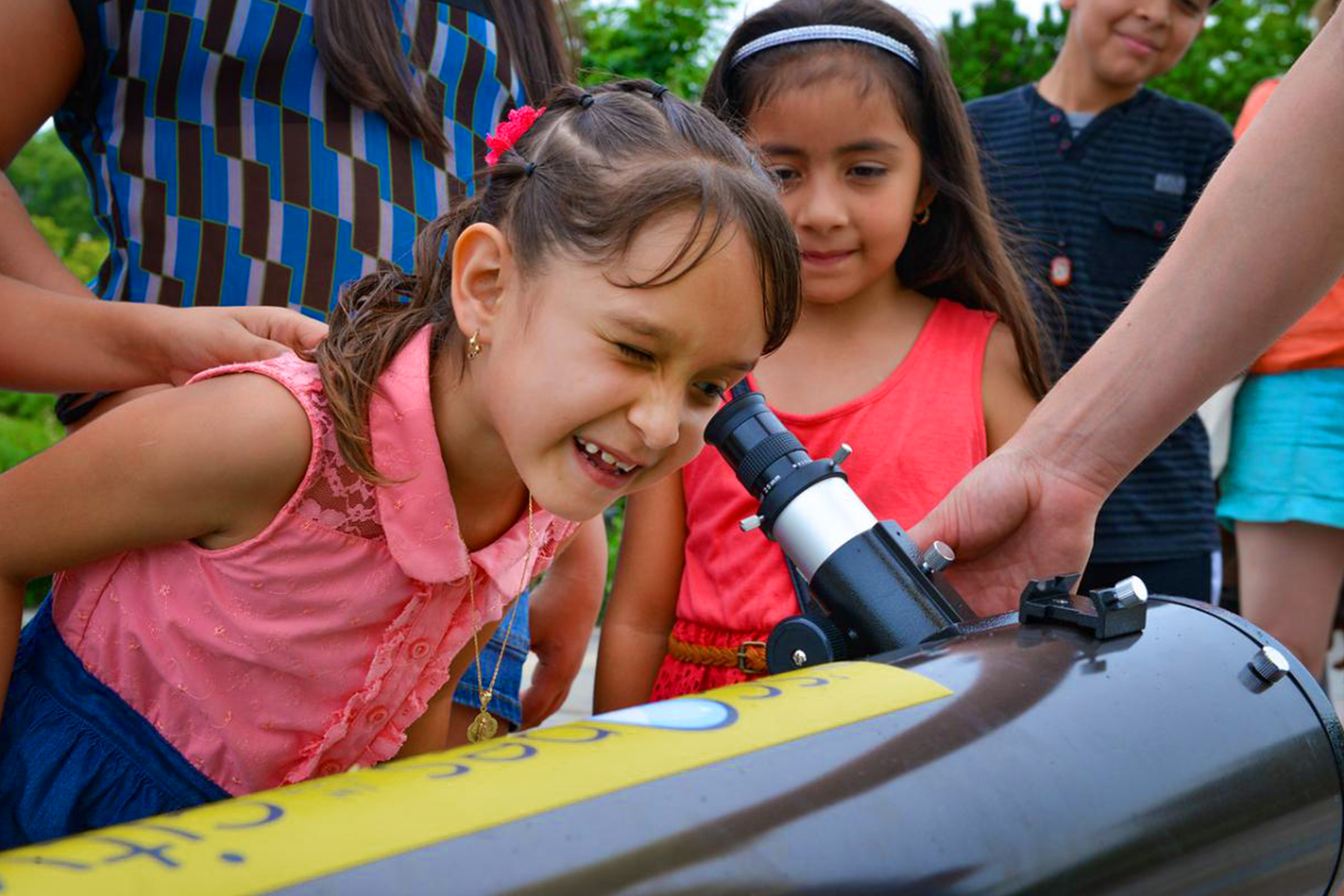 A young girl looks into a telescope as other watch.