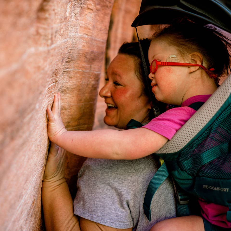 Featured Contributor, Melody Forsyth (left), backpacks with her daughter, Ruby (right), as they touch some rock formations.