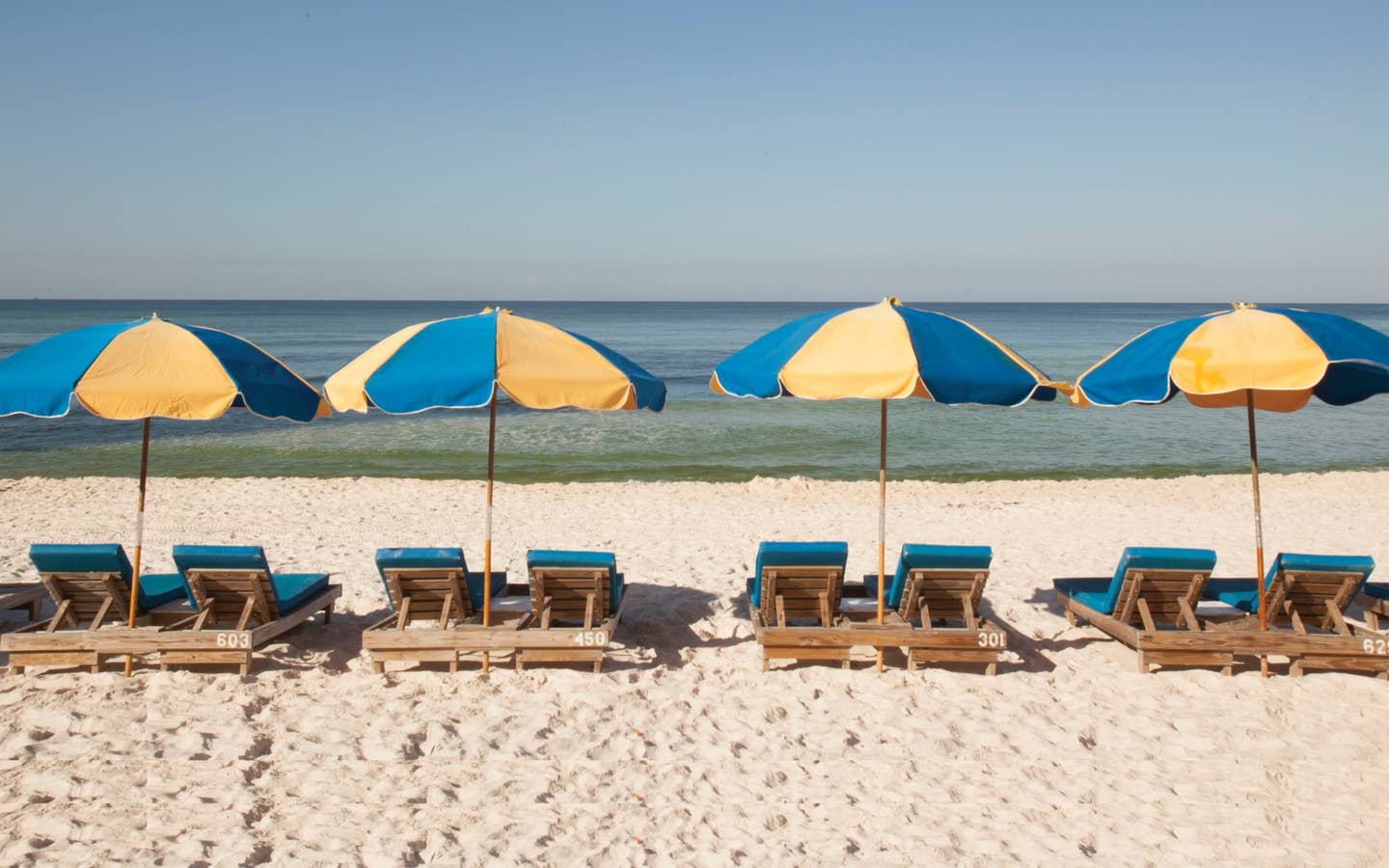 View of four beach chairs under two umbrellas at Panama City Beach in Florida.