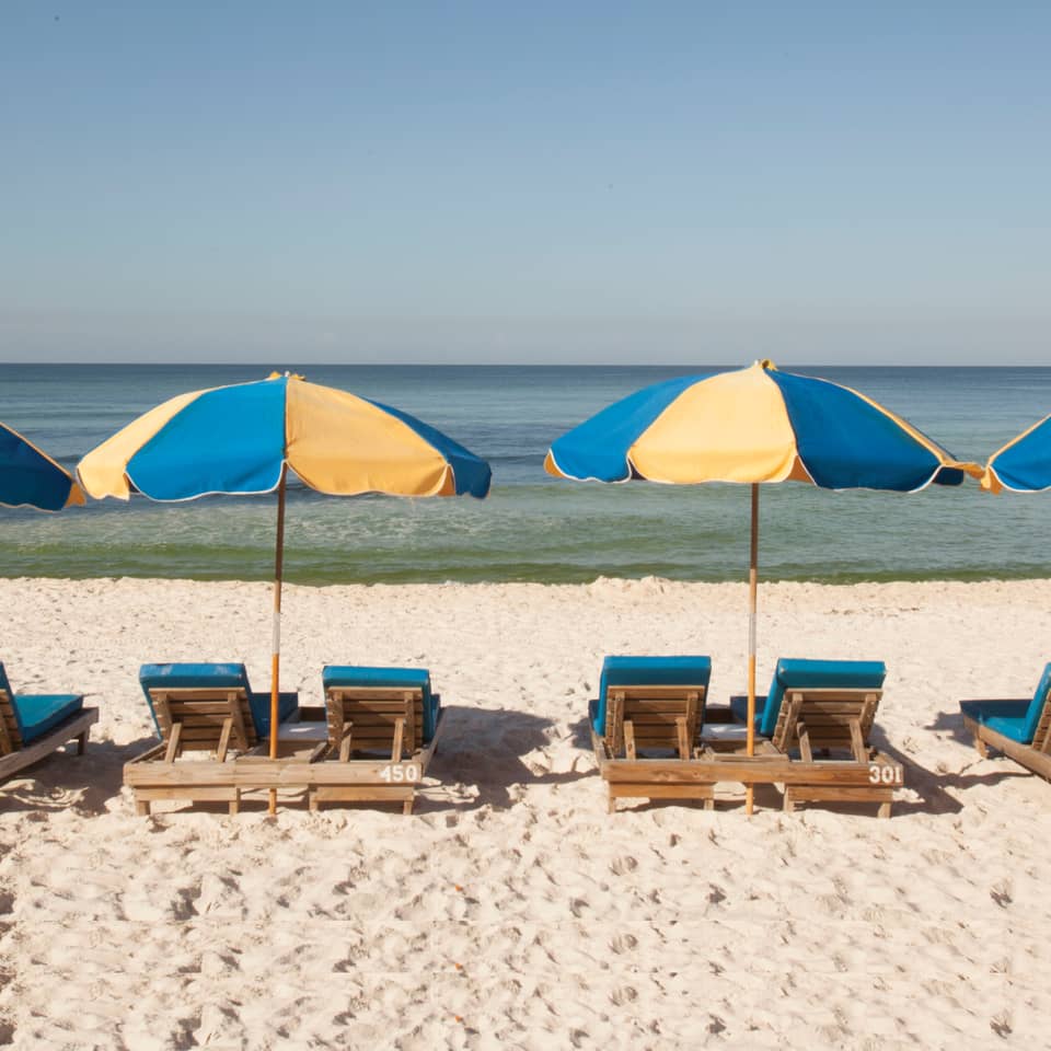 View of four beach chairs under two umbrellas at Panama City Beach in Florida.