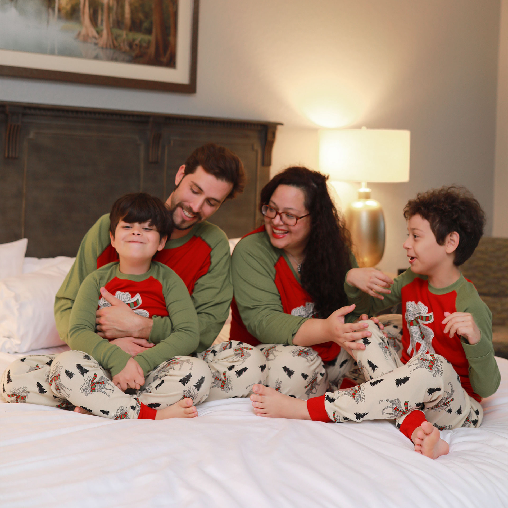 Two young boys, a man and woman wear matching pajamas on a bed.
