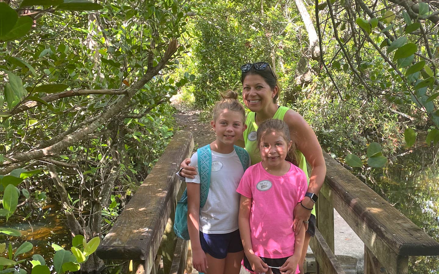 A caucasian woman (middle) poses with two young caucasian girls (front) on a wooden bridge in the Everglades.