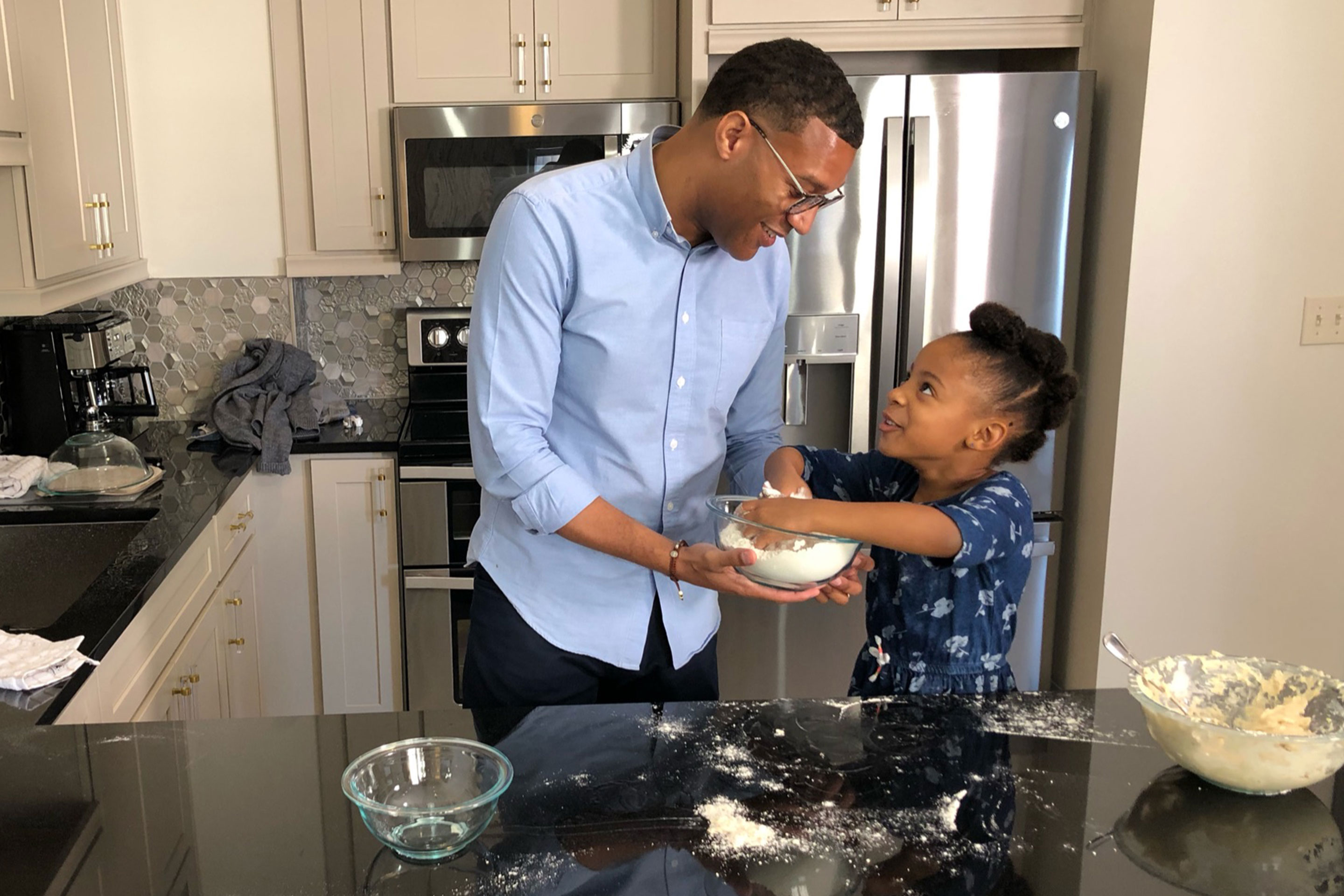 A father in a blue dress shirt (left) and his daughter (right in navy dress) make beignets together in our signature villa kitchen in our resort in New Orleans, Louisiana.