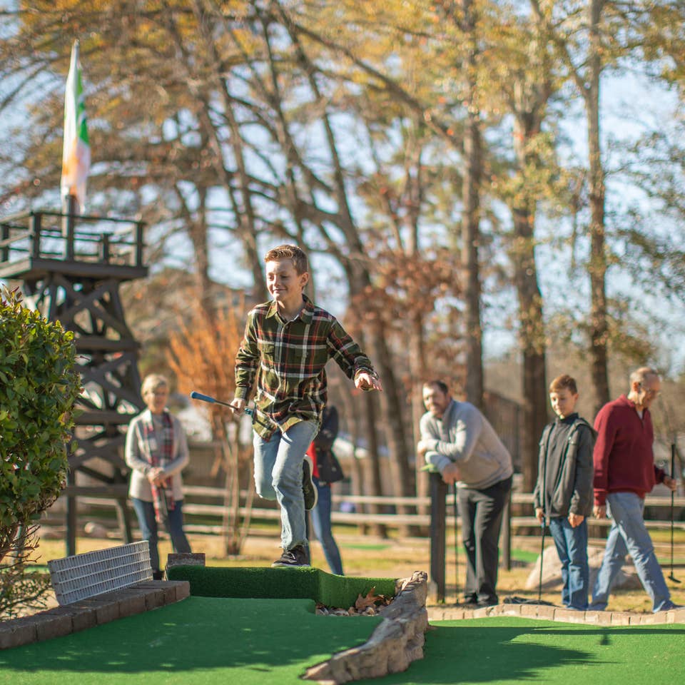 Family playing mini golf with fall foliage in the background at Villages Resort in Flint, Texas.