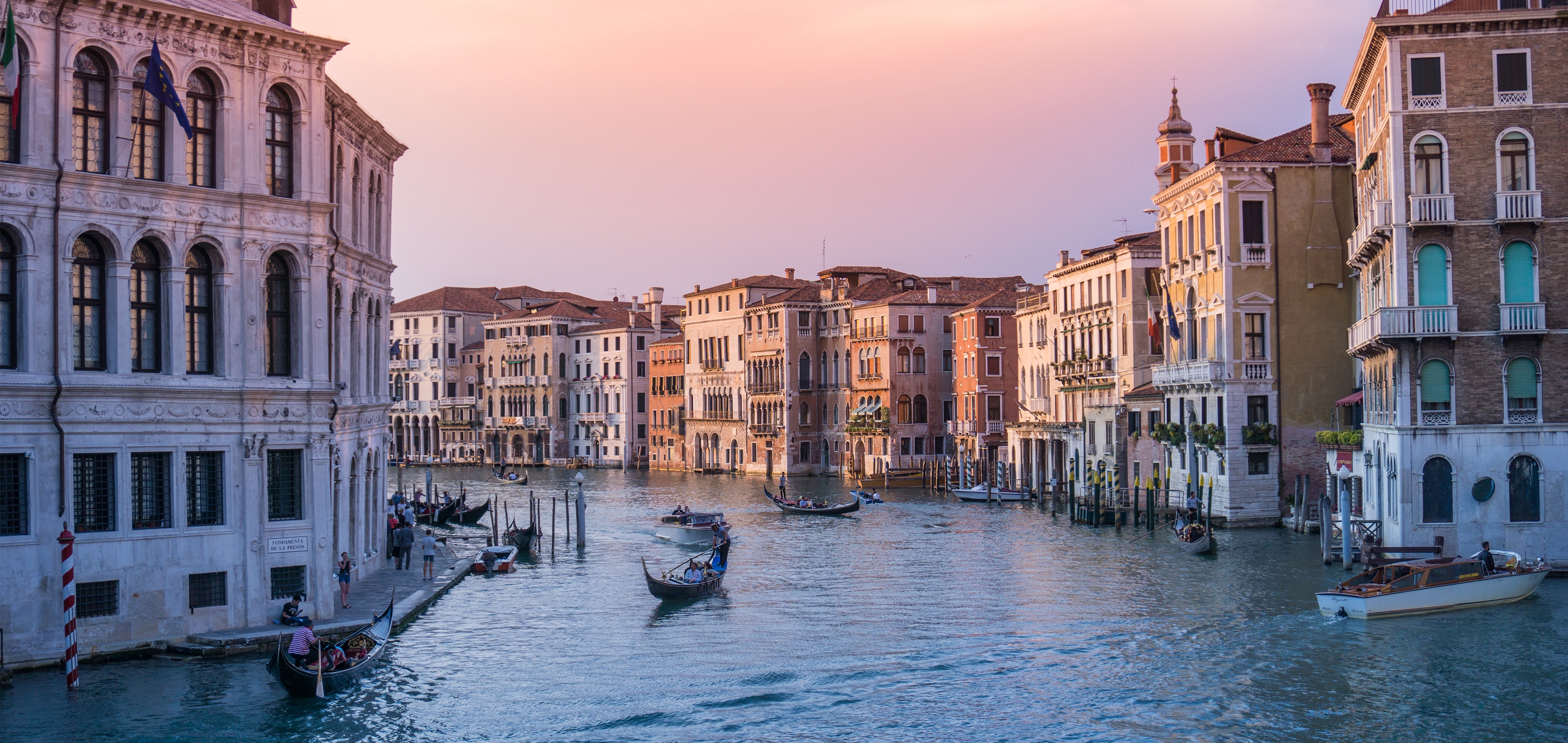 The rivers of Venice with gondolas and structures under sunset pink skies.