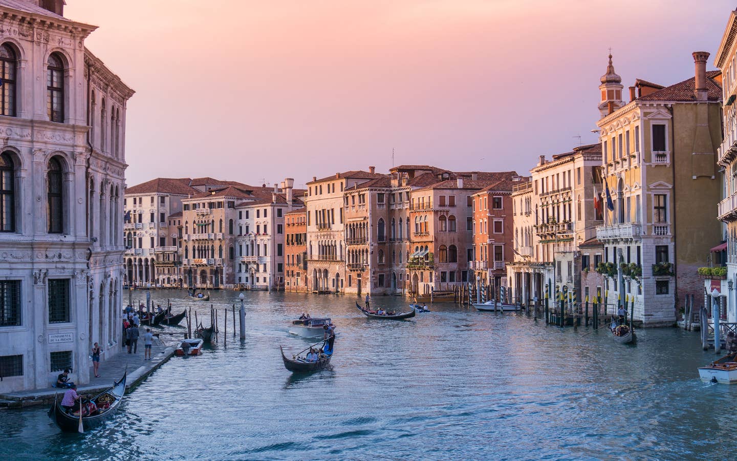The rivers of Venice with gondolas and structures under sunset pink skies.