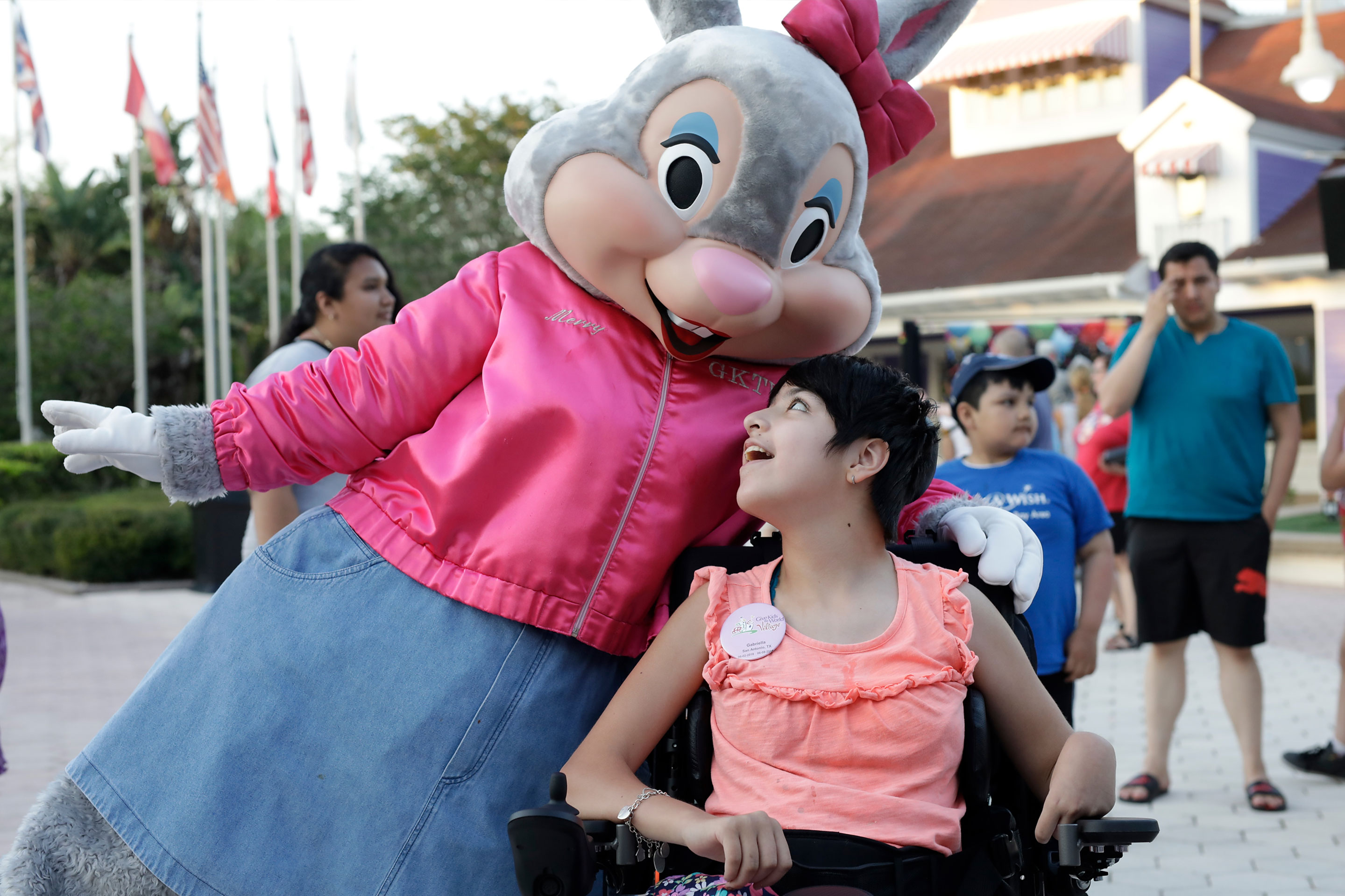 Miss Merry the Bunny (left) wears a pink coat and bow as she embraces a young villager in a wheelchair (right).