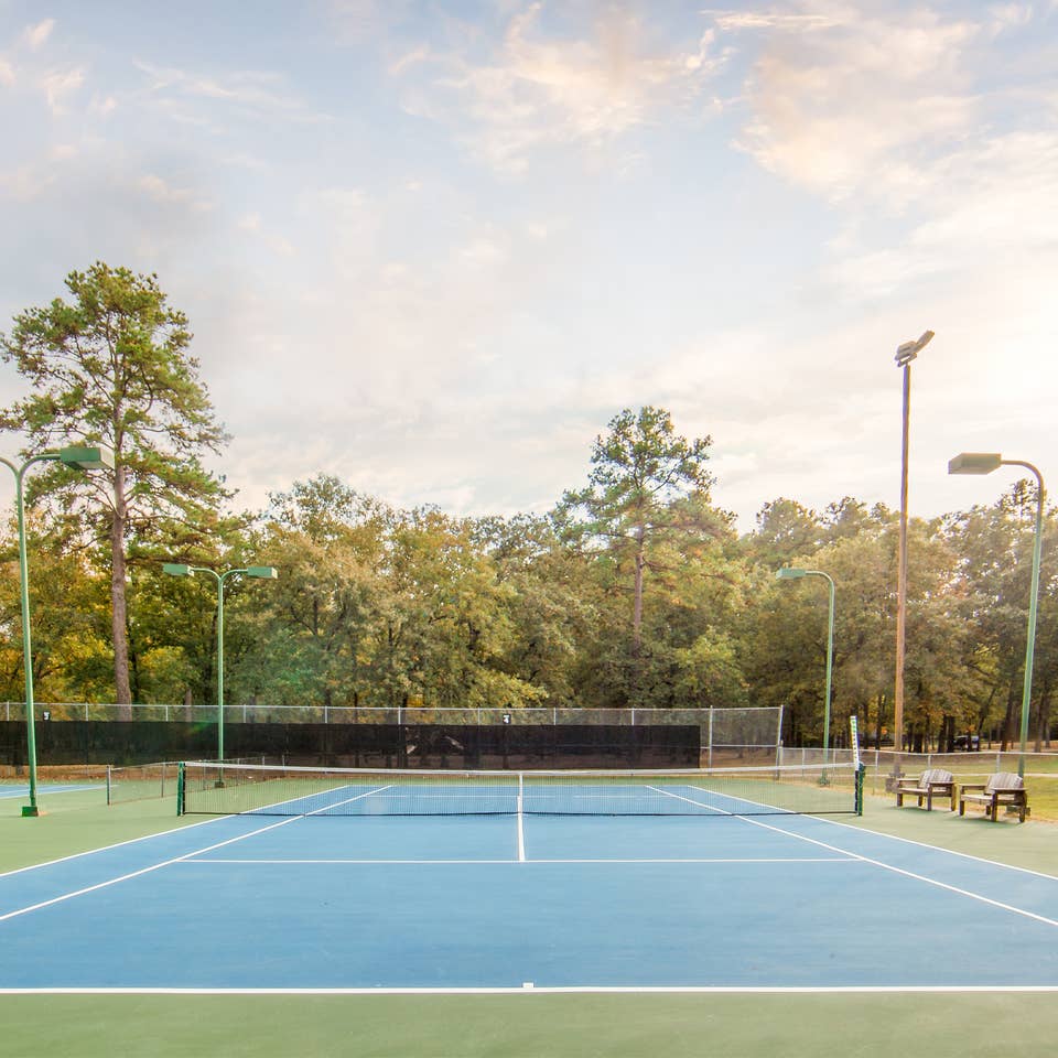 Outdoor tennis court surrounded by trees at Holly Lake Resort in Texas.