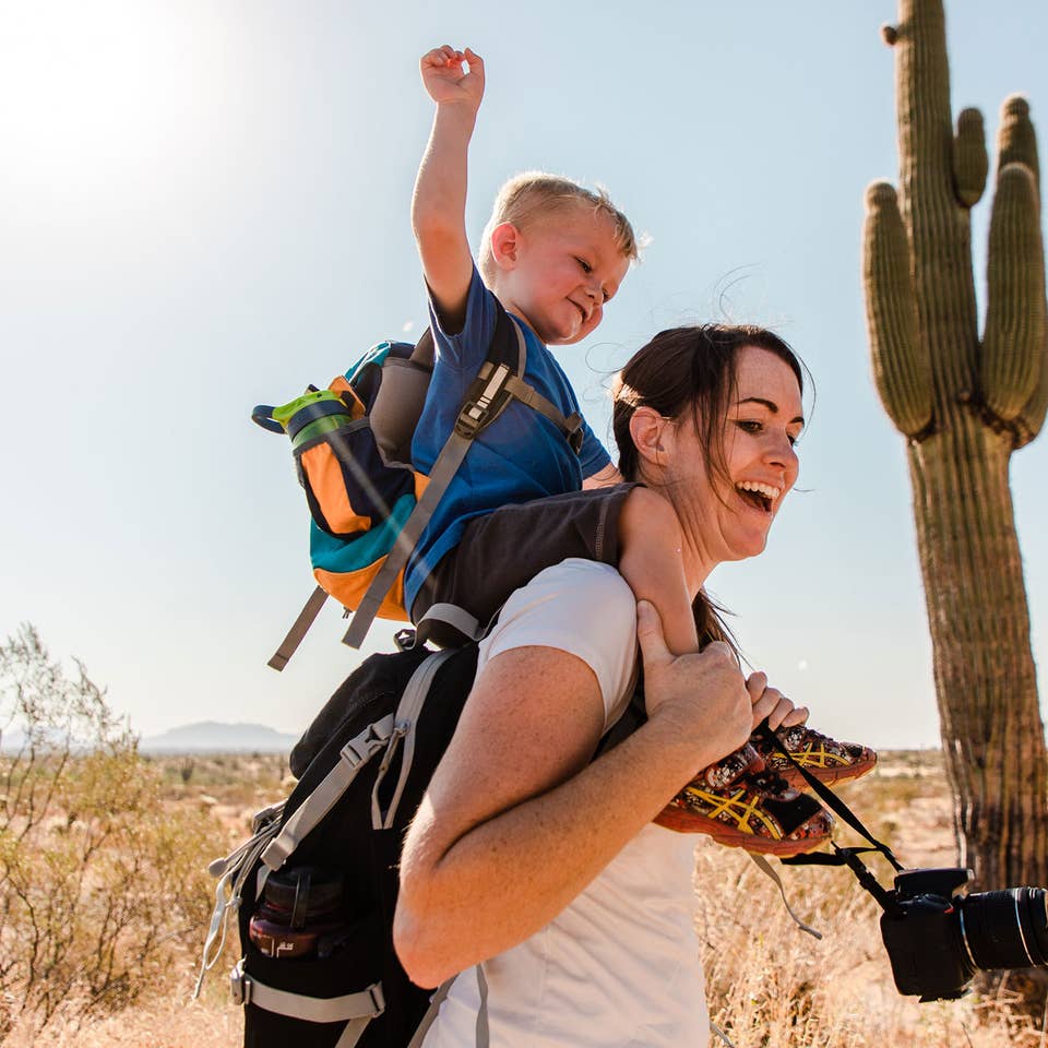 Jessica and her son laughing together while he sits on her shoulders as they hike in the Arizona desert.