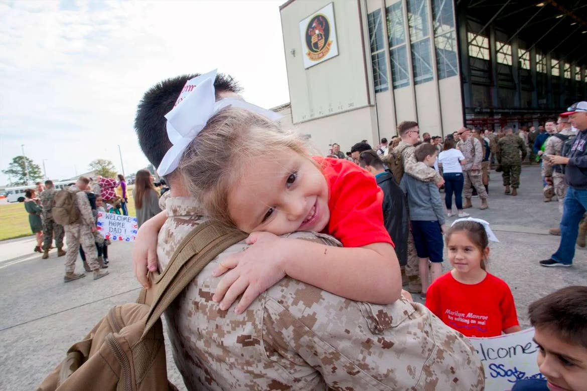 Sara Perez's youngest daughter (right) is held by her dad in his uniform outside of an air hangar.