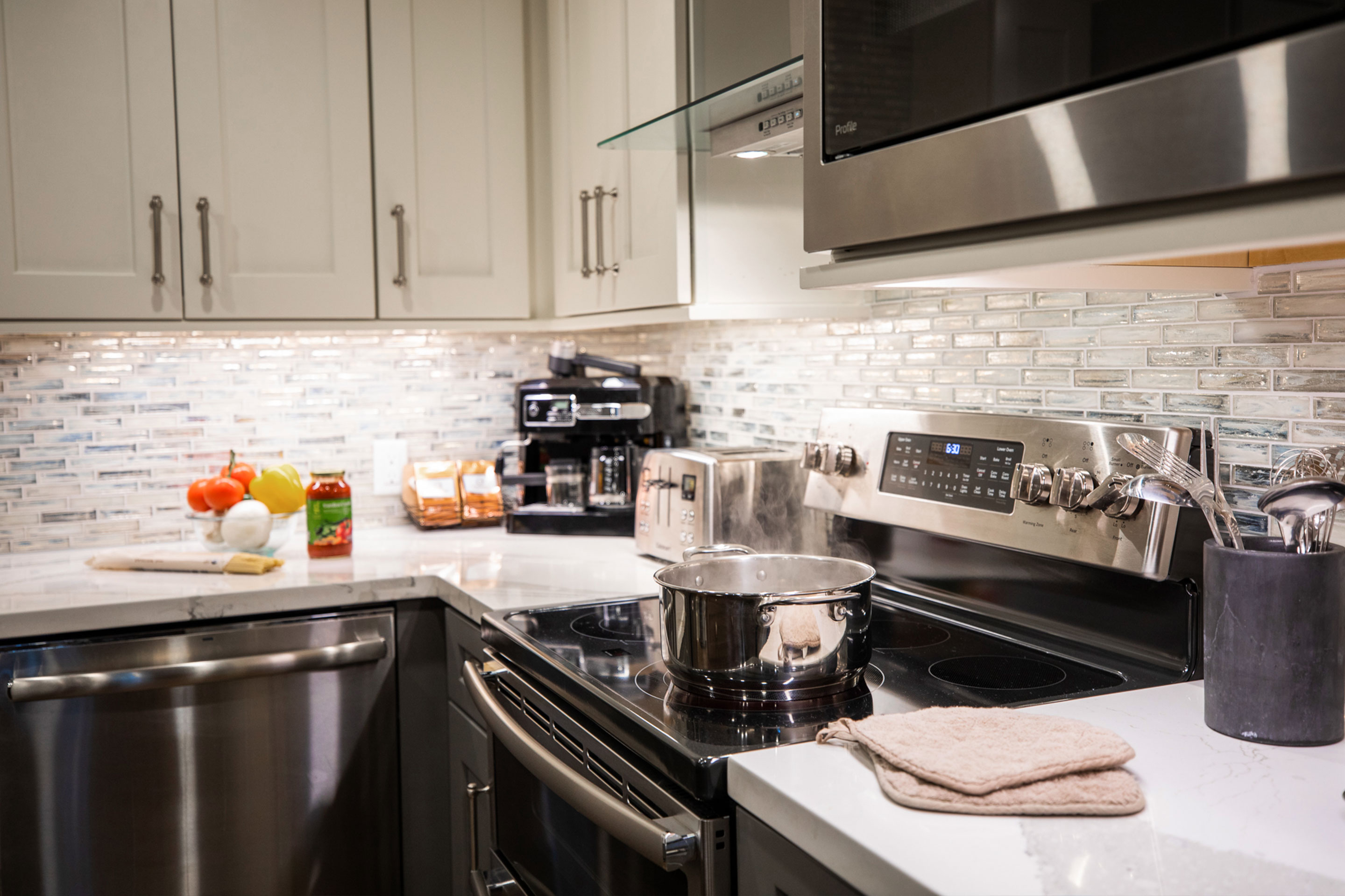 A kitchen countertop with spaghetti ingredients and noodles being boiled on a stovetop.