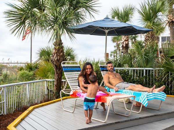 Two adults and child sitting under pool umbrella at Beach Club at South Beach Resort in Myrtle Beach, South Carolina.