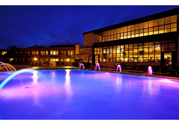 Evening view of a resort's illuminated pool area, featuring colorful lights reflecting off the water.