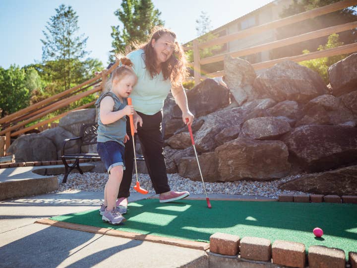Mother and daughter playing mini golf outdoors at Oak n' Spruce Resort in South Lee, Massachusetts.
