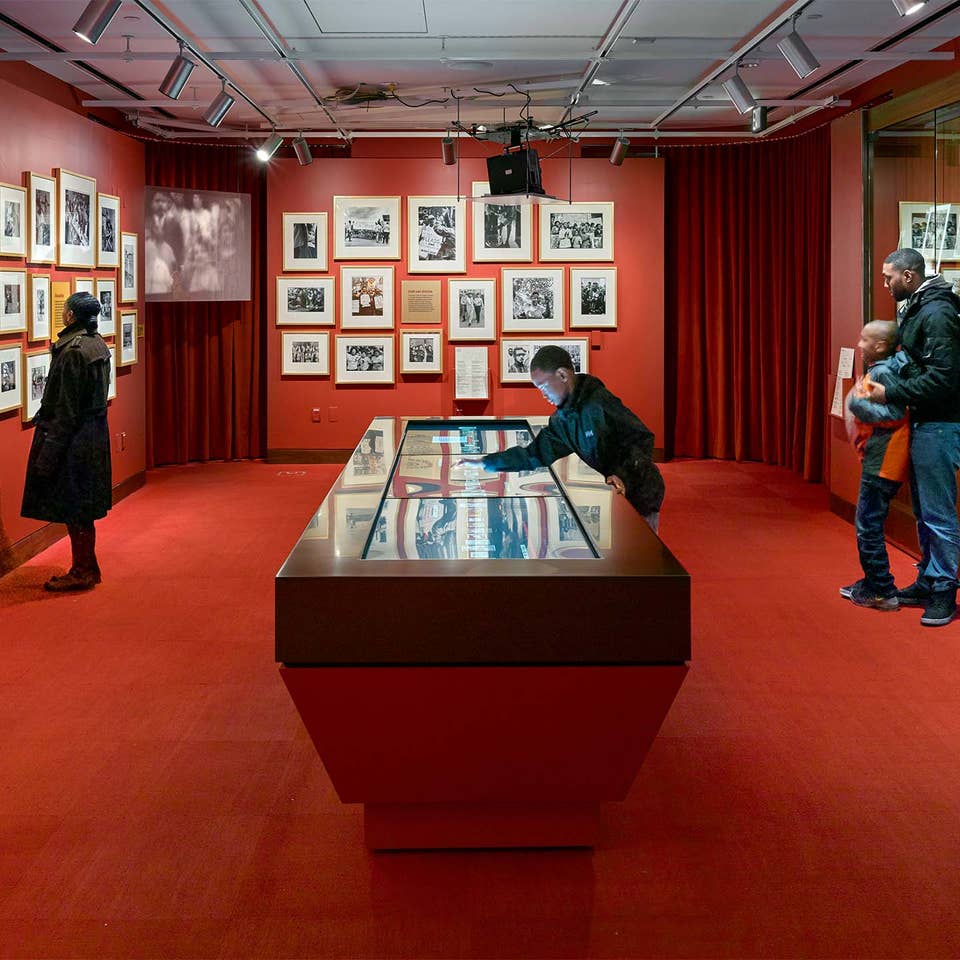A woman, two young boys and a man stand in a red room curated with photography and video displays.