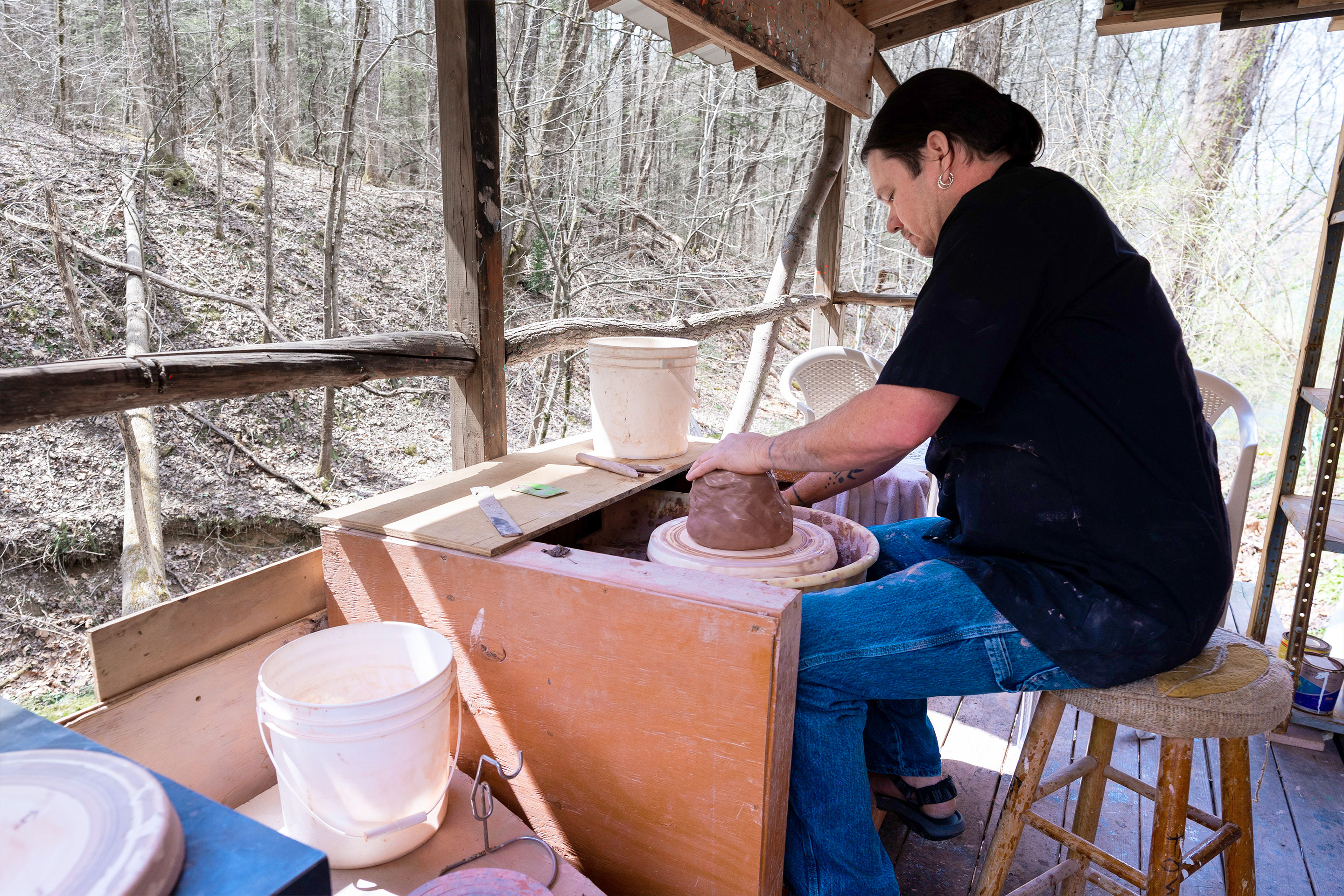 A man works with clay pottery outdoors while wearing a black shirt and jeans at Fowler's Clay Works.