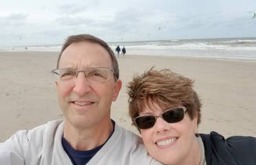 A man (left) wears a light grey crewneck sweater next to a woman (right) on a beach in Zandvoort, Netherlands.