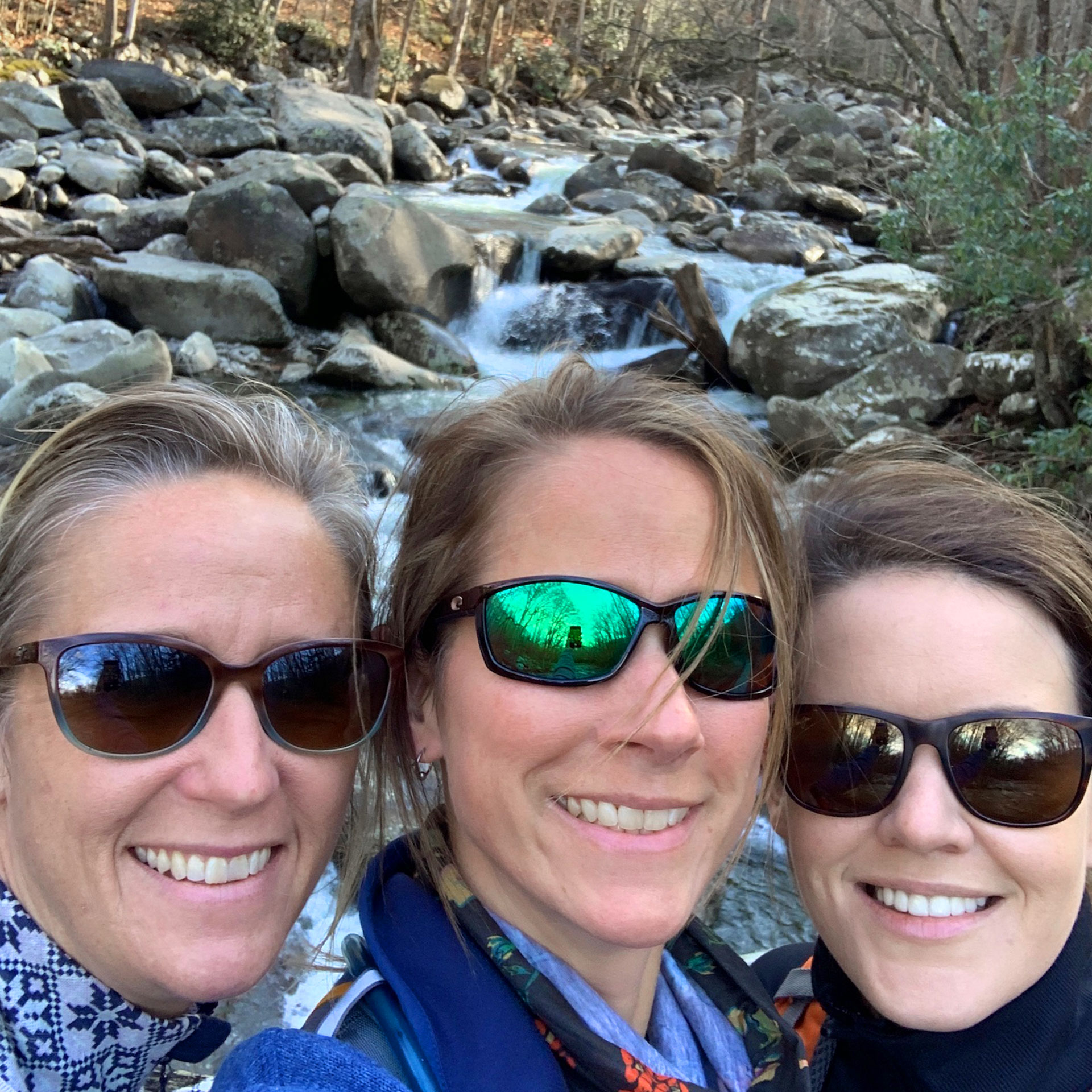 Featured Contributor, Jennifer C. Harmon (right) and her two girlfriends wear sunglasses in front of a waterfall.