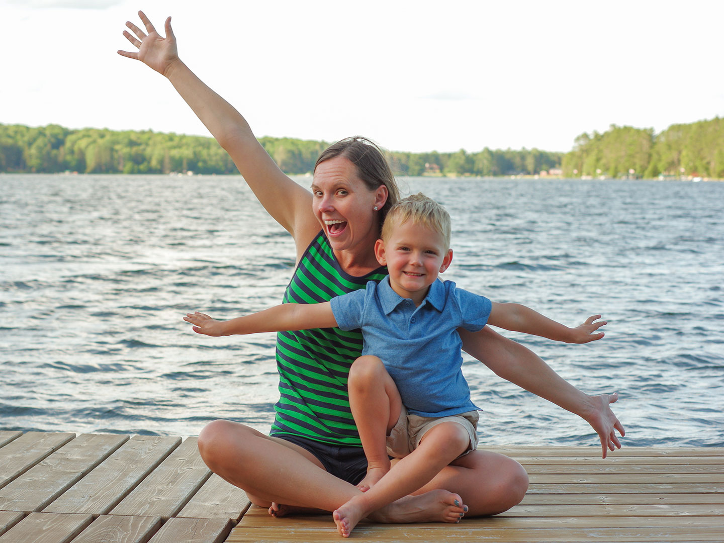 Author, Sarah Conroy, and son, Logan, sit on a lake pier mimicking an airplane with their arms.
