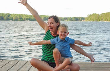 Author, Sarah Conroy, and son, Logan, sit on a lake pier mimicking an airplane with their arms.