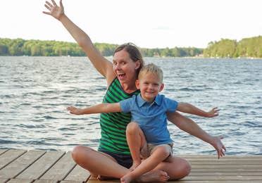 Author, Sarah Conroy, and son, Logan, sit on a lake pier mimicking an airplane with their arms.