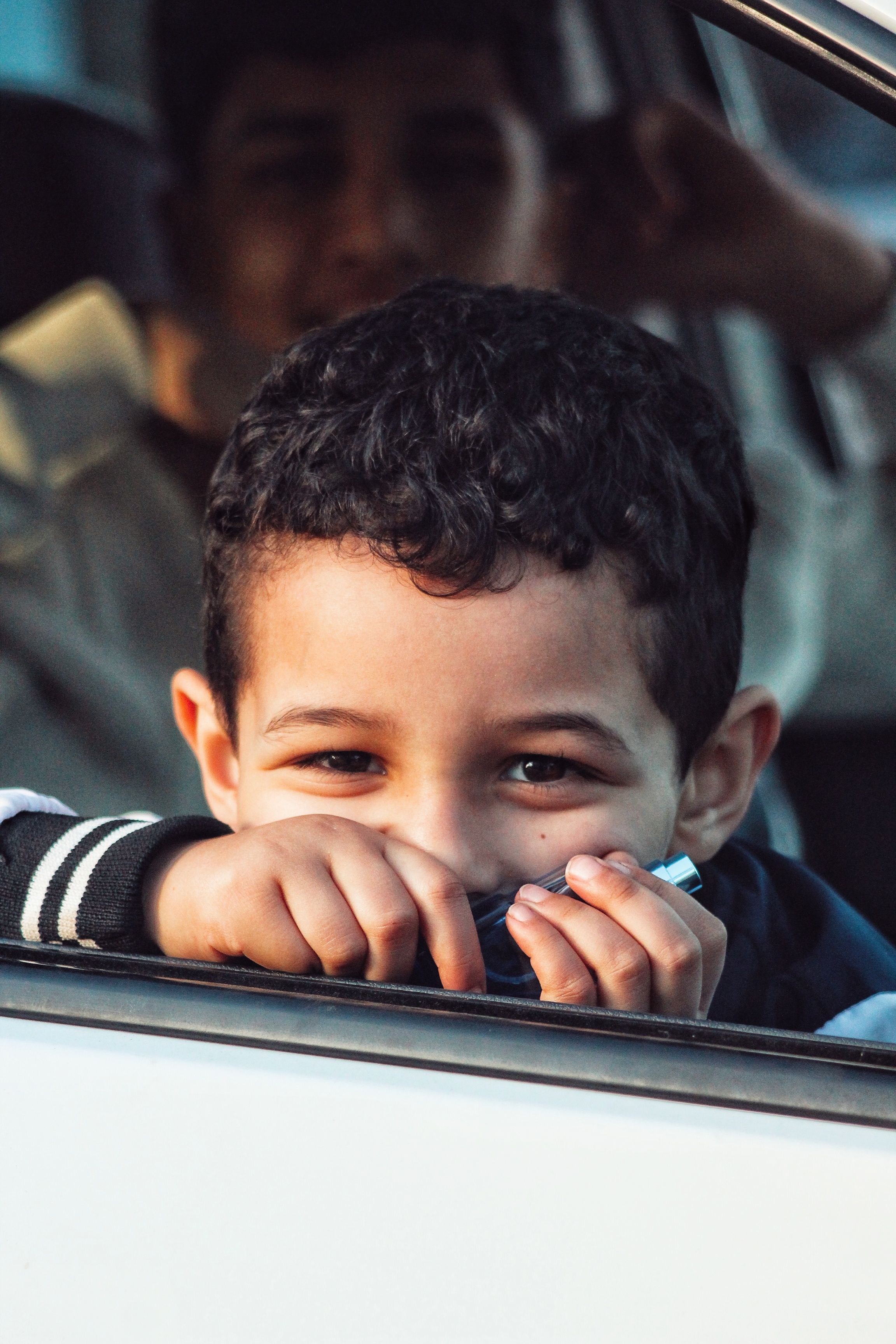 Child looking out car window with parent behind. 