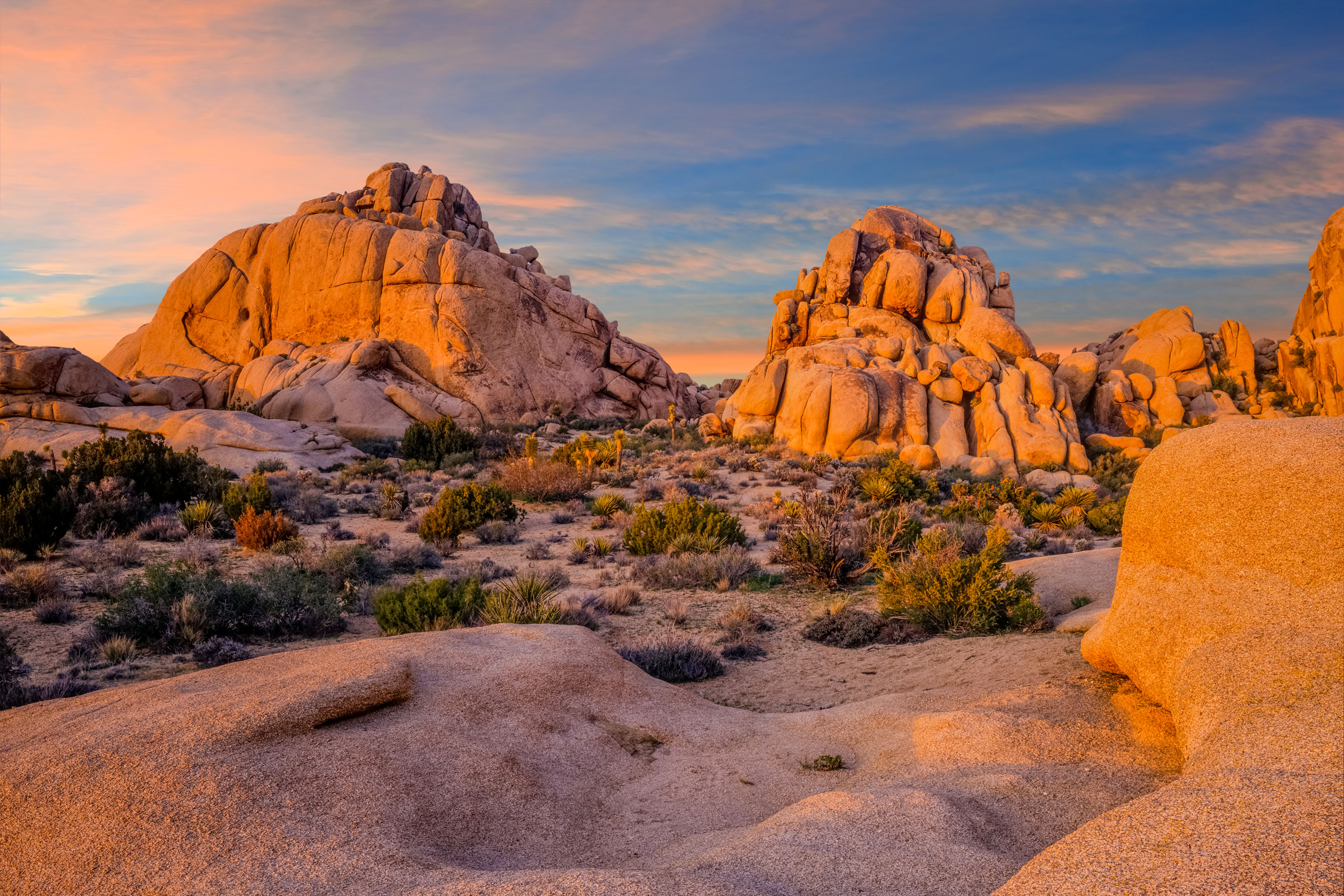Rock boulder formations in a dessert under a sunset, and blue sky.