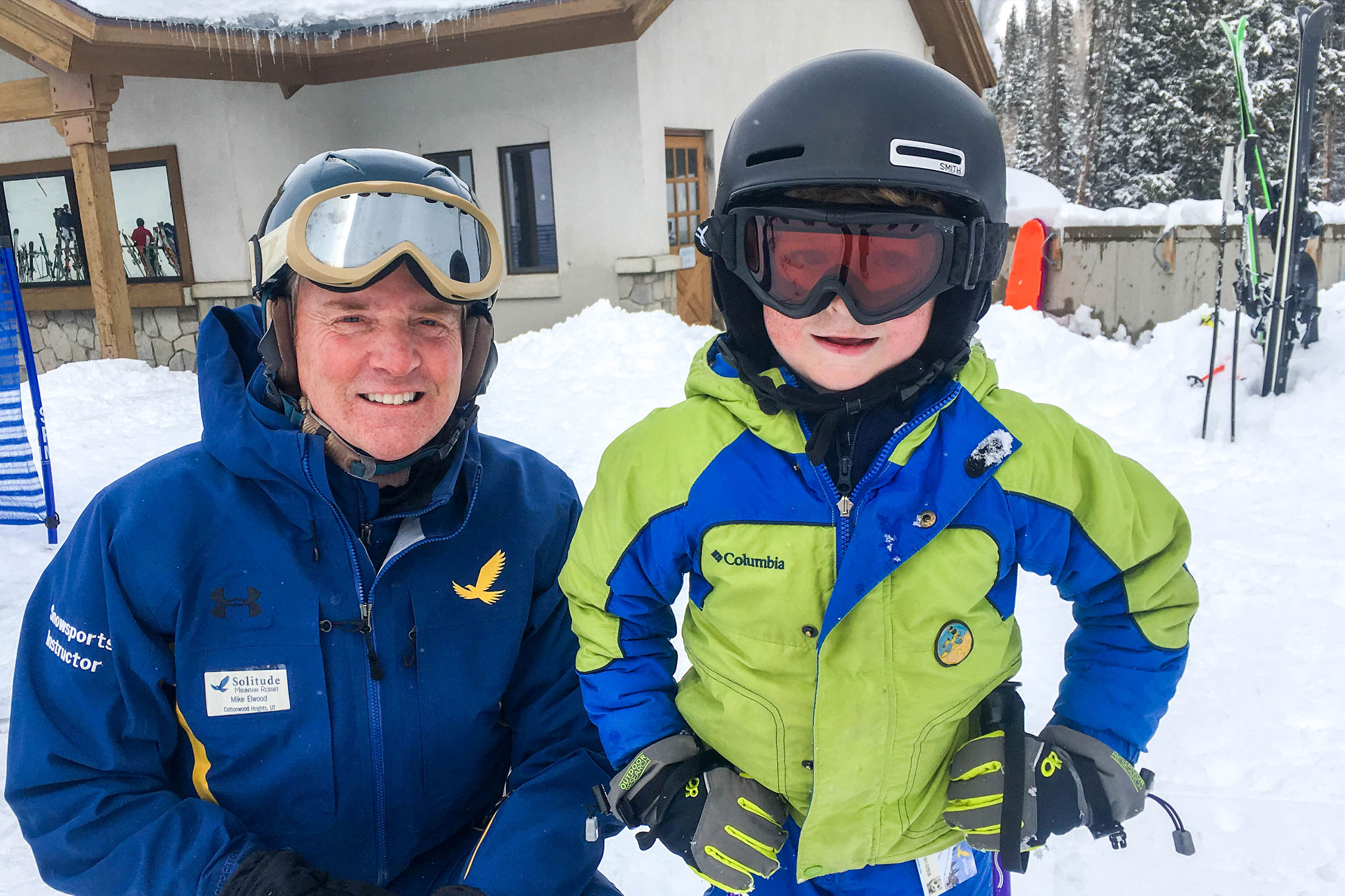 Jessica's son stands next to a Resort Employee wearing their winter and skiing gear.